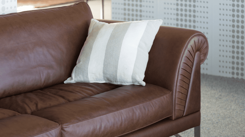 Image of brown leather couch with throw pillow in corner.